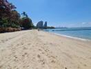 Serene beachfront with clear skies, sandy shores, and lush greenery near residential high-rises