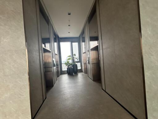 Modern hallway with marble floors and sleek mirrored walls leading to a well-lit room