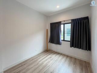 Spacious and well-lit empty bedroom with wooden flooring and large window