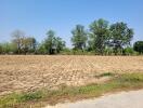 Spacious undeveloped land with dry, plowed soil and scattered trees under a clear sky