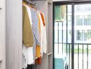 Modern entryway with an open wardrobe featuring stylish clothes and a view to the balcony