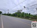 View of vacant land beside a paved road with streetlights and power lines