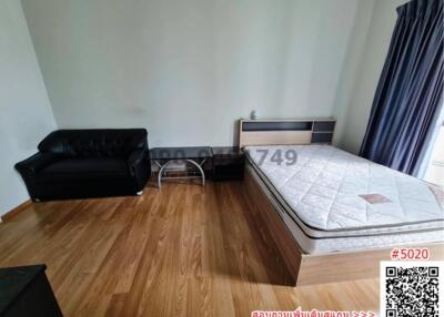 Spacious bedroom with wooden flooring, black sofa, and large mattress
