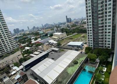 Panoramic city view from a high-rise apartment balcony showing nearby buildings, a swimming pool, and distant cityscape