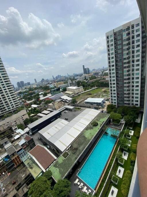 Panoramic city view from a high-rise apartment balcony showing nearby buildings, a swimming pool, and distant cityscape