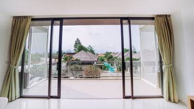 Spacious bedroom with large sliding doors opening to a balcony overlooking a pool and lush greenery