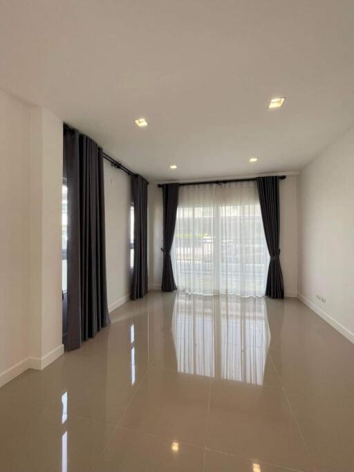 Spacious and well-lit living room with glossy tiled flooring and elegant curtains