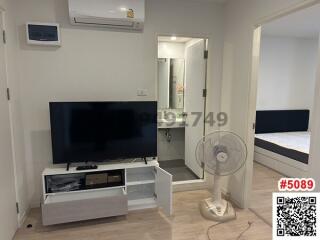 Modern living room with mounted television, white entertainment unit, and glass door leading to bedroom