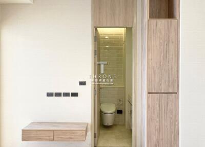 Modern entryway with sleek wooden features leading to a well-lit bathroom