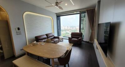 Modern living room with cityscape view featuring a brown leather sofa set and a wooden dining table