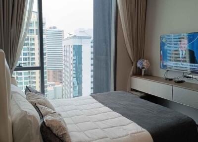 Modern bedroom with city view through large windows and a television