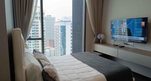 Modern bedroom with city view through large windows and a television