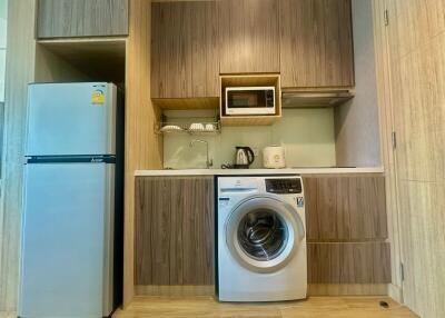 Compact modern kitchen with wooden cabinets, washing machine, and essential appliances