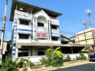 White and blue three-story building with a traditional facade and a sign in Thai script