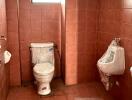 Clean bathroom with terra cotta tiles, equipped with toilet and urinal
