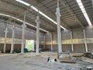 Spacious industrial warehouse interior with high ceiling and construction debris