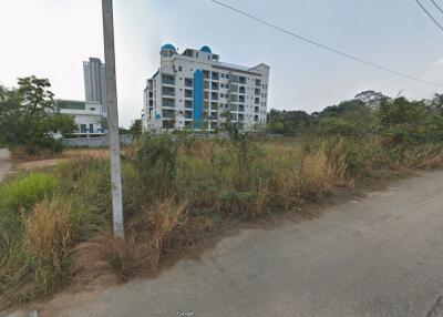 View of a modern condominium building from a nearby overgrown field