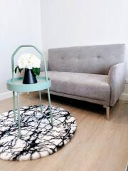 Modern living room with grey sofa, stylish marble pattern rug, and mint side table with a vase of white flowers