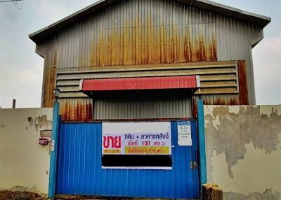 Exterior view of a rustic commercial warehouse with a weathered blue gate and rusted metal sheet facade