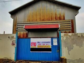 Exterior view of a rustic commercial warehouse with a weathered blue gate and rusted metal sheet facade