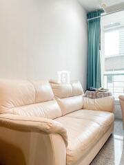 Spacious and bright living room with a modern beige leather sofa and large window with teal curtains