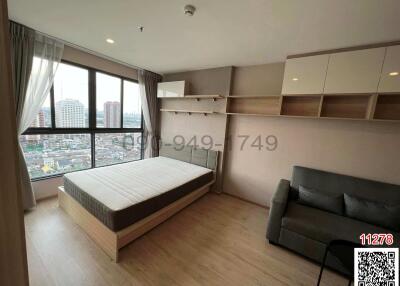 Modern bedroom with city view, including a queen-sized bed and a gray sofa