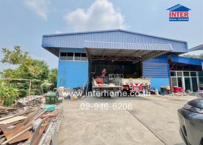 Industrial warehouse with blue walls and a front yard cluttered with materials