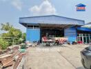 Industrial warehouse with blue walls and a front yard cluttered with materials