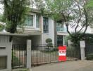 Contemporary two-story house with lush greenery and a for-sale sign