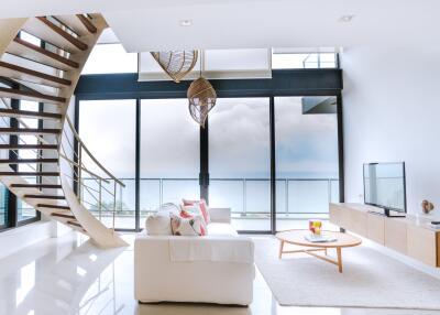 Luxurious open plan living room with sea view, large windows, spiral staircase, and minimalist decor