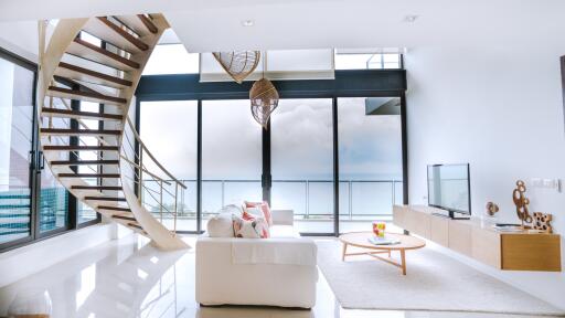 Luxurious open plan living room with sea view, large windows, spiral staircase, and minimalist decor