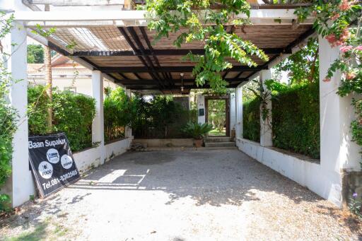 Covered driveway entrance with lush greenery and a welcoming path leading to the main door