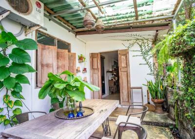 Airy outdoor dining area with natural wood table and lush green plants