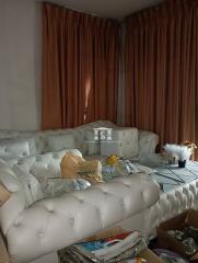 Cluttered living room with white leather sofa and heavy curtains