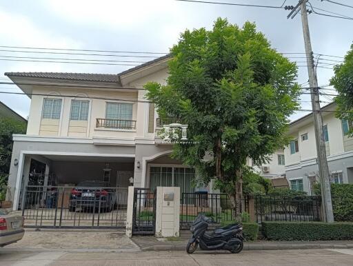 Two-story residential house with gated entrance and lush greenery