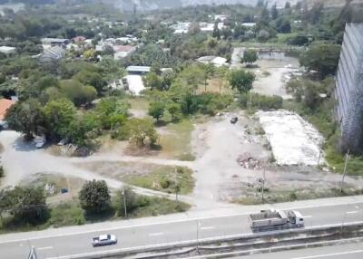 Aerial view of a property near a highway featuring a large vacant lot surrounded by some greenery and developed buildings