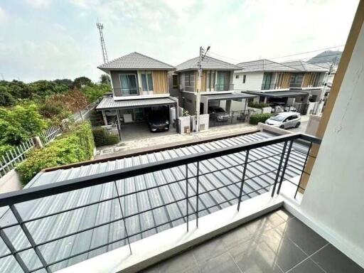 View of a residential neighborhood from a balcony showing houses with metal roofs and cars parked