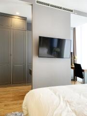 Modern bedroom with wall-mounted TV and view into dining area