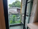 View of a small balcony with open sliding door, overlooking green outdoor area