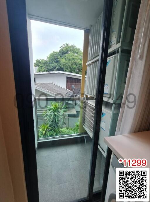 View of a small balcony with open sliding door, overlooking green outdoor area