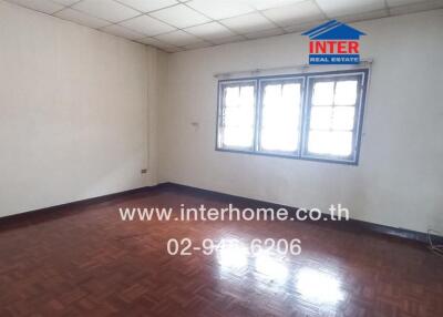 Empty bedroom with wooden floors, windows, and white walls