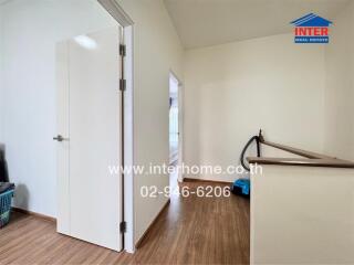 Brightly lit hallway with wooden flooring and open door leading to another room