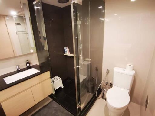 Modern bathroom with glass shower, wooden vanity, and well-lit mirror