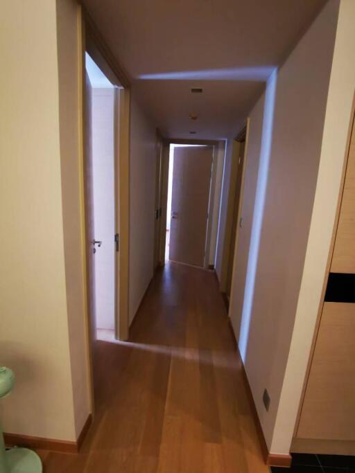 Narrow residential hallway with wooden flooring and multiple doors