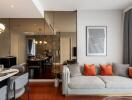 Modern living room with grey sofa and vibrant orange cushions, along with a dining area in the background