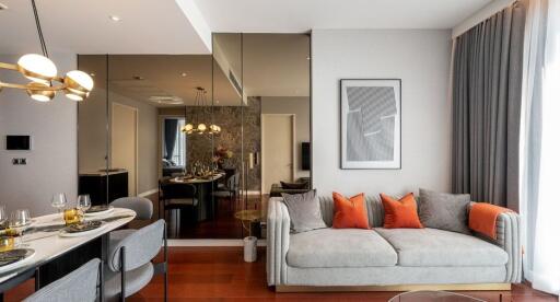 Modern living room with grey sofa and vibrant orange cushions, along with a dining area in the background
