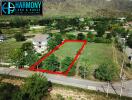 Aerial view of a spacious land plot outlined in red, adjacent to a main road, with surrounding lush greenery and a mountain backdrop