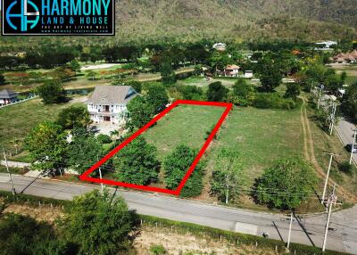 Aerial view of a spacious land plot outlined in red, adjacent to a main road, with surrounding lush greenery and a mountain backdrop