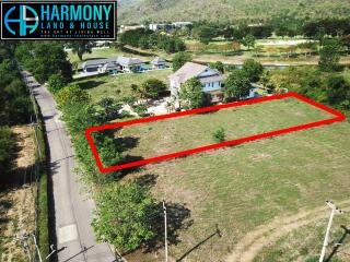 Aerial view of a spacious land plot for sale surrounded by greenery, near residential buildings and a road