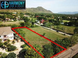 Aerial view of a land plot outlined in red, bordering a road with a scenic backdrop of mountains and houses